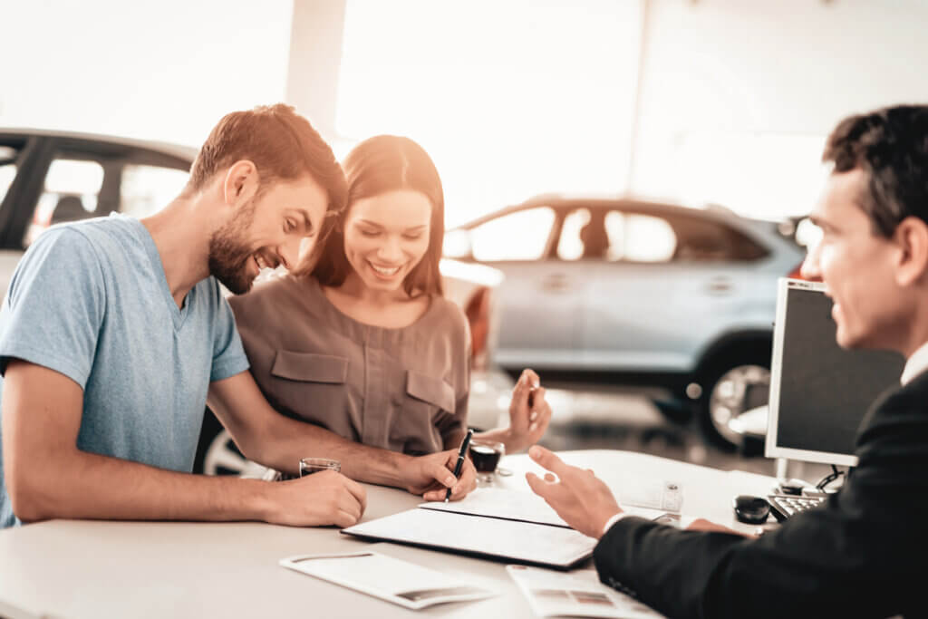 Pareja feliz firmando papelería de compra de un auto usado
